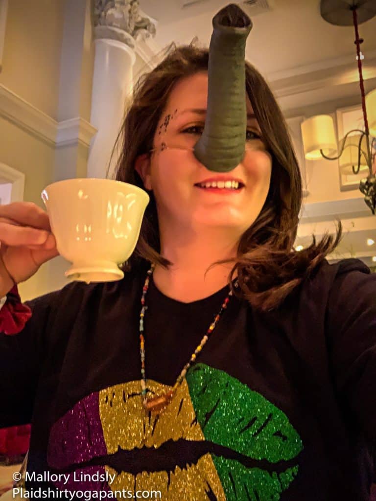 A girl with brown hair, drinking tea, wearing a glitter lips shirt and a elephant nose